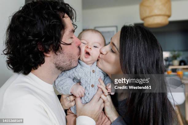father and mother kissing baby boy at home - baby father hug side stock pictures, royalty-free photos & images