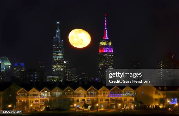 Percent waning gibbous moon rises behind the Empire State Building and One Vanderbilt in New York City and homes in the neighborhood of Society Hill...