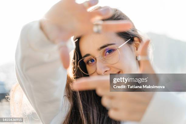 portrait of beautiful young woman in white sweatshirt in sunny day, white color. hands frame on foreground. - portrait blurred background stockfoto's en -beelden