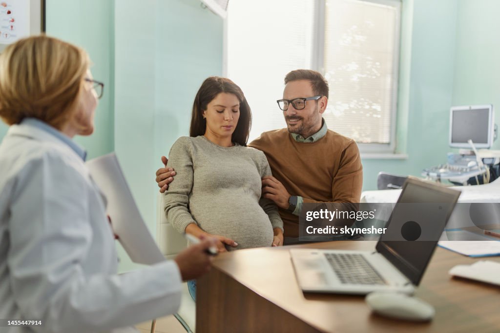 Young pregnant couple talking to gynecologist in the office.