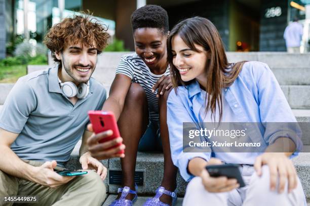 multiracial young adult people having fun watching funny social media content on smartphone app while relaxing together outdoors - meme stock pictures, royalty-free photos & images