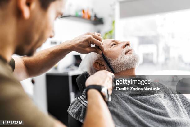 senior man at barber getting his beard trimmed with electric razor - beard trimming stock pictures, royalty-free photos & images