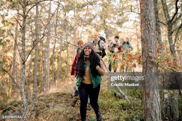 happy male and female friends hiking together amidst trees in forest - fall hiking stock pictures, royalty-free photos & images