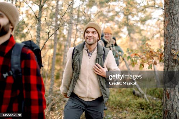 smiling man wearing warm clothing while hiking with friends in forest - forest walking front stock pictures, royalty-free photos & images