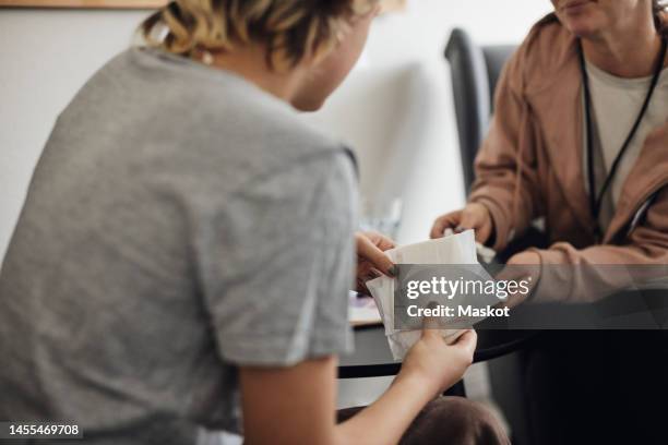 teenage female student holding sanitary pads while talking to counselor in school office - menstruation photos et images de collection