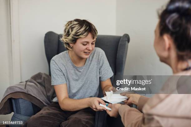 smiling female students taking sanitary pads and tampons from non-binary counselor in school office - tampon stock pictures, royalty-free photos & images