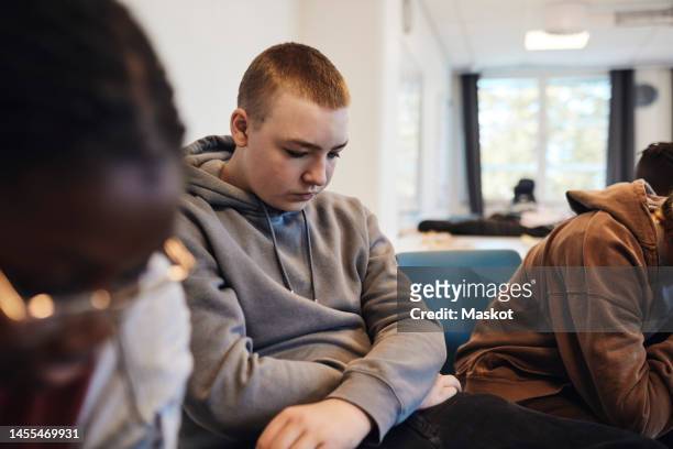depressed teenage boy with short hair sitting amidst female friends in group therapy at school - teen group therapy stock pictures, royalty-free photos & images