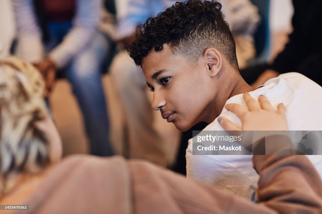 Teenage boy looking at female friend consoling in group therapy
