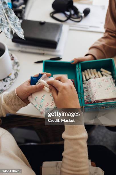 hands of female student holding sanitary pads and tampons at table in school office - tampon menstruation stock-fotos und bilder