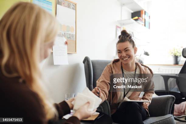 happy non-binary counselor discussing with female student holding sanitary pads in school office - girl using tampon ストックフォトと画像