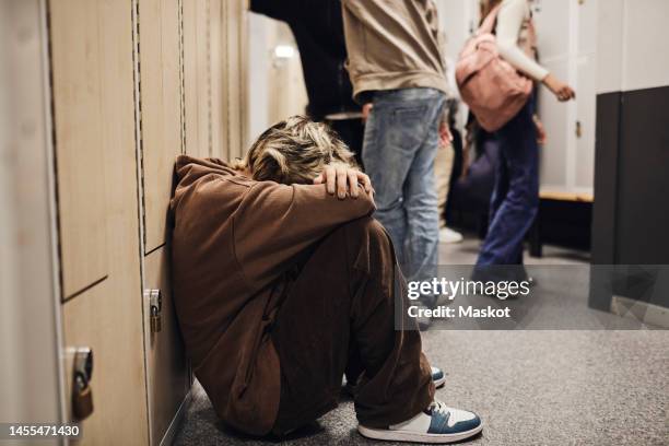 full length of sad teenage girl sitting in school corridor - violencia escolar fotografías e imágenes de stock