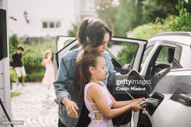 mother teaching daughter to plug charger in electric car - electric car charger imagens e fotografias de stock