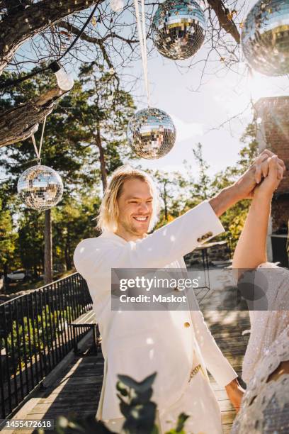 happy groom holding bride's hand dancing under disco balls on sunny day - front on groom and bride stock pictures, royalty-free photos & images