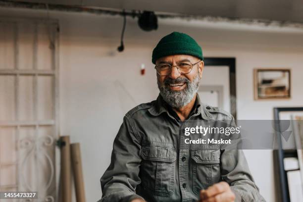 portrait of cheerful male owner wearing knit hat and eyeglasses in workshop - man and portrait imagens e fotografias de stock