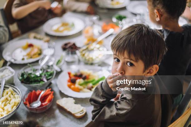 portrait of boy covering mouth with hand with breakfast on table at day care center - sweden school stock pictures, royalty-free photos & images