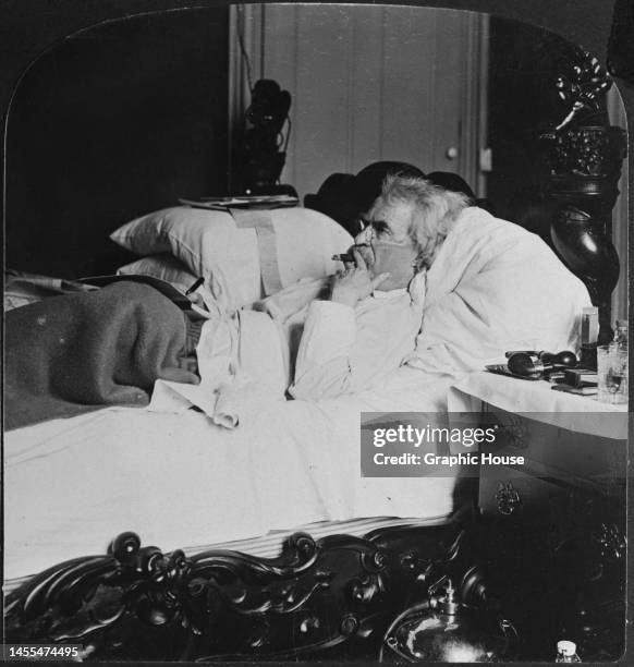 American writer and humourist Mark Twain lying in bed, smoking a cigar as he writes in a notebook, at his home in Hartford, Connecticut, circa 1890....