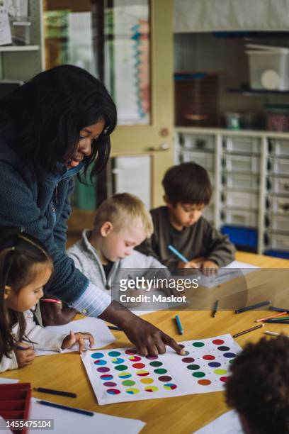 female teacher guiding students to recognize colors while training them in day care center - child care worker stockfoto's en -beelden