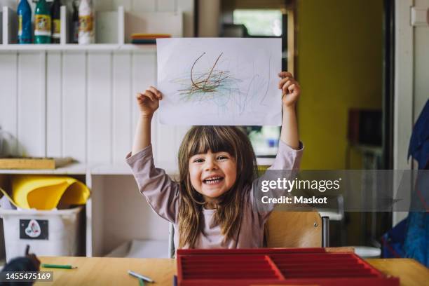 portrait of happy girl showing color pencil scribble on paper at kindergarten - kids drawing stock-fotos und bilder