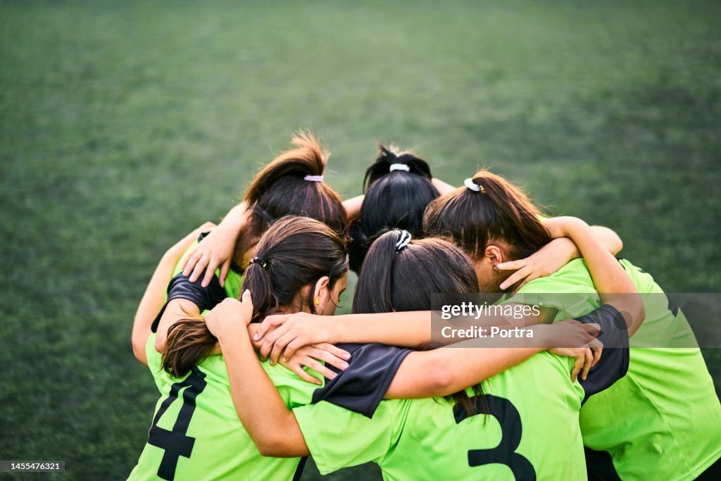 Girls soccer team discussing game plan in a huddle on field