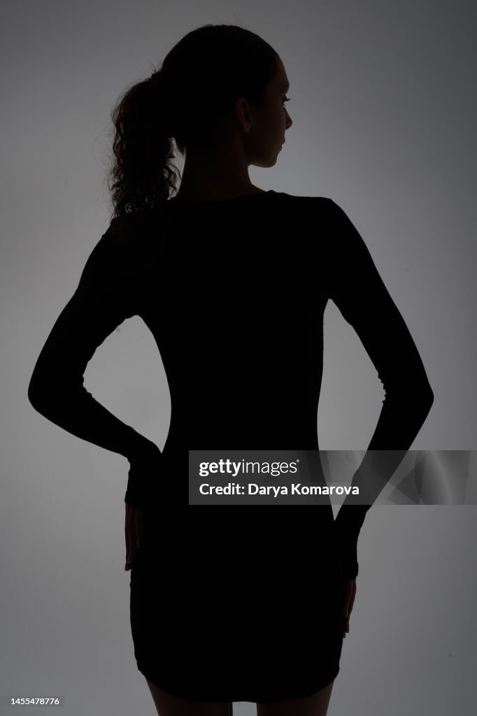 A beautiful young woman is in the shadow. A portrait with a light on the face with copy space. The profile of woman from behind with beautiful figure.