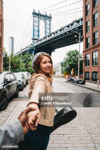 une femme rousse tient les mains de son mari, lui disant de la suivre - manhattan bridge photos et images de collection