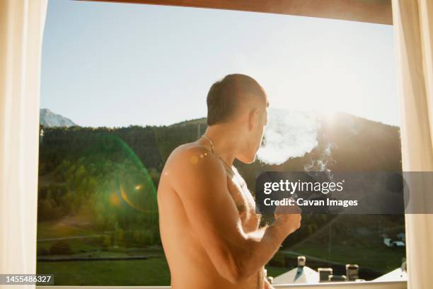 shirtless guy smoking a marijuana joint on the terrace in the morning - joint body part stock-fotos und bilder