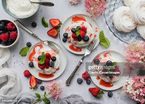 overhead of mini pavlova meringue cakes with fresh berries and cream - whipped cream stock pictures, royalty-free photos & images