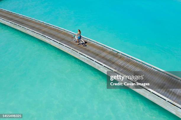 aerial view of young woman riding by bicycle on jetty in the sea - thulusdhoo stock pictures, royalty-free photos & images