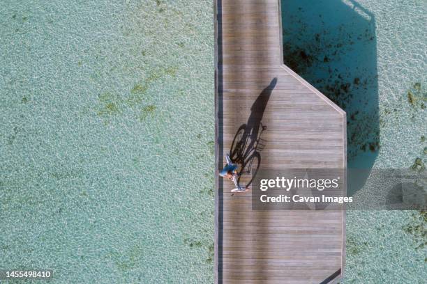 aerial view of young man riding by bicycle on jetty in the sea - thulusdhoo stock pictures, royalty-free photos & images