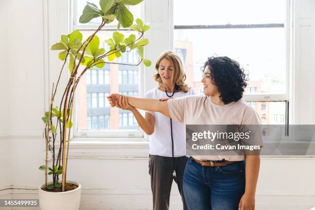 doctor guiding patient while doing exercise in clinic - gp practice stock pictures, royalty-free photos & images