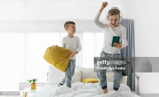 hermanos divirtiéndose con la tecnología. - a boy jumping on a bed fotografías e imágenes de stock