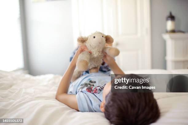 boy laying on bed with stuffed animal - stuffed toy stock pictures, royalty-free photos & images