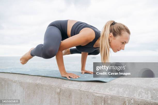 a girl on the seashore doing yoga frog pose - woman frog hand stockfoto's en -beelden