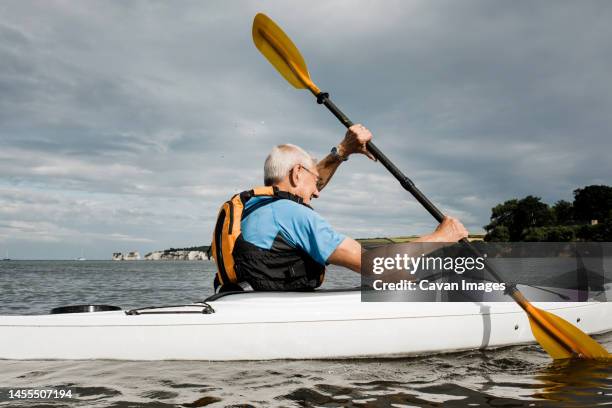 retired man kayaking in the sea exercising at the beach - seniors canoeing stock pictures, royalty-free photos & images