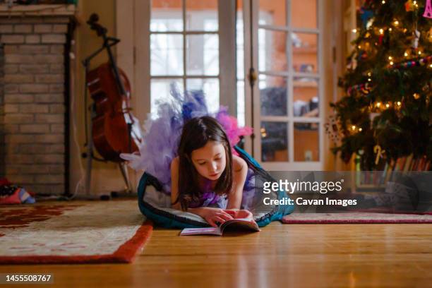 a small girl in tutu reads on floor by christmas tree - child christmas costume stock pictures, royalty-free photos & images