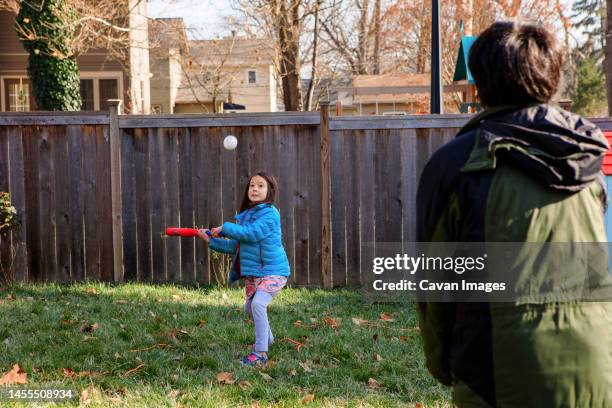 a little girl plays softball with father in backyard in winter - backyard baseball stock-fotos und bilder