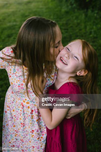big sister kisses and hugs little sister while she smiles and laughs - preadolescent kind 個照片及圖片檔