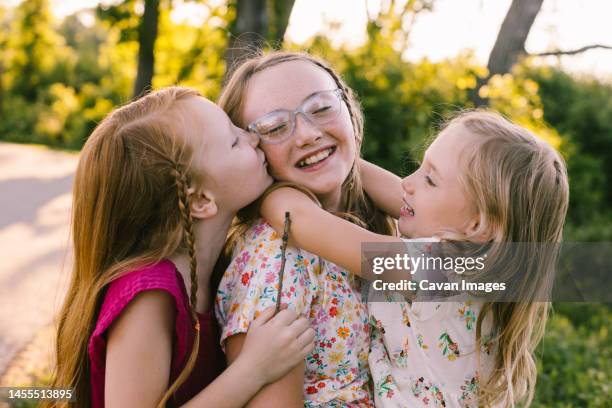 young sisters laugh, hug and kiss in golden light - kids kindness stock pictures, royalty-free photos & images