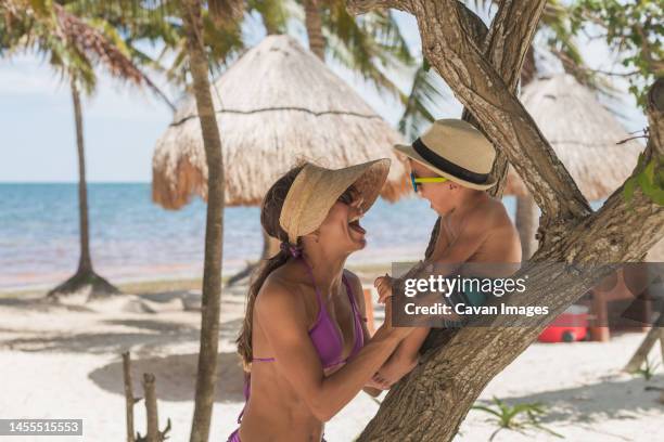 young mother with her son playing on a tree at the beach and smiling - cancun fotografías e imágenes de stock