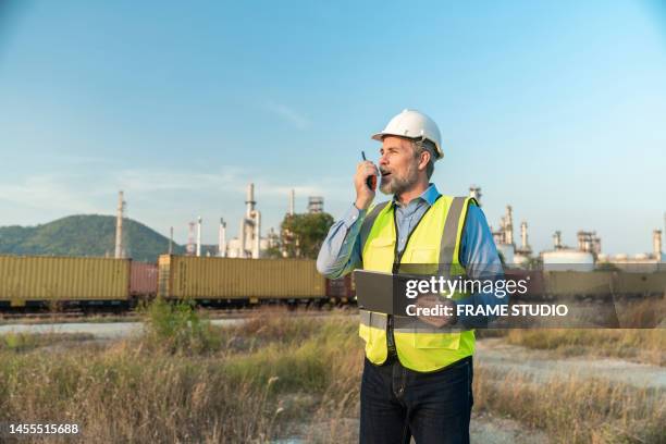 refinery managers or senior oil chemical engineers use tablet ipads and are using radio communications to communicate the ingenuity and cutting-edge of refineries and energy. it has a transportation train in front and an oil refinery in the background. - gas plant stock pictures, royalty-free photos & images