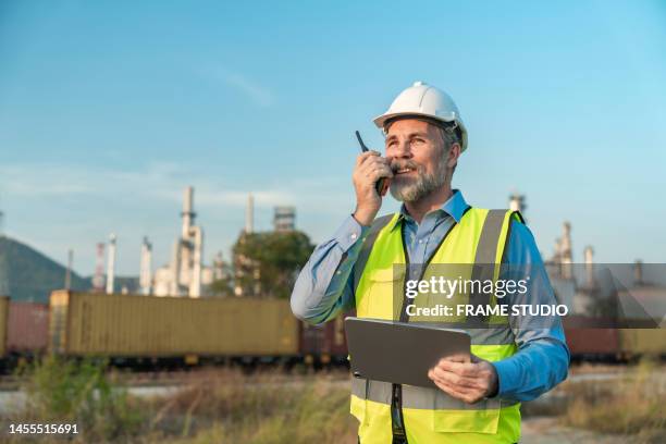 refinery managers or senior oil chemical engineers use tablet ipads and are using radio communications to communicate the ingenuity and cutting-edge of refineries and energy. it has a transportation train in front and an oil refinery in the background. - gas plant stock pictures, royalty-free photos & images