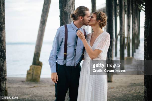 newlyweds kissing together on beach in the redwoods, california, - small wedding stock pictures, royalty-free photos & images