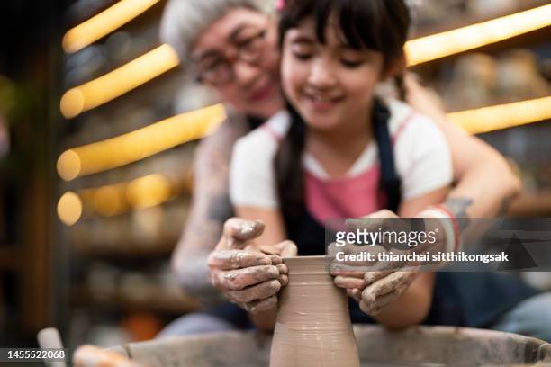 woman teaching little girl to making pottery on a pottery wheel in studio. - learning generation parent child stock pictures, royalty-free photos & images