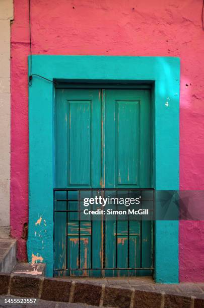 metal barred double doorway of a colonial house painted pink and light blue - double door stock-fotos und bilder