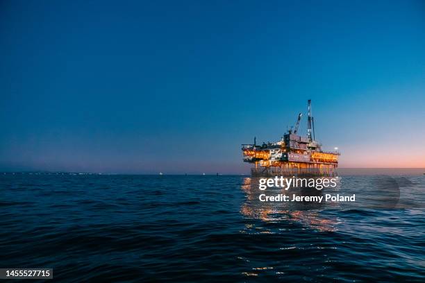 low wide angle image of an off-shore oil rig at dusk off the coast of huntington beach with copy space - oil production platform stock pictures, royalty-free photos & images