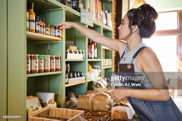 young woman working in a cafe arranging the products on display rack - boulangerie vitrine stockfoto's en -beelden
