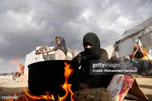 Yemeni displaced mother prepares a meal for her children outside their shelter at an internally displaced camp on January 10, 2023 near Amran...