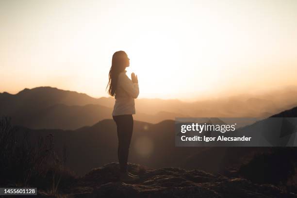 woman meditating at sunset in the mountains - budismo imagens e fotografias de stock