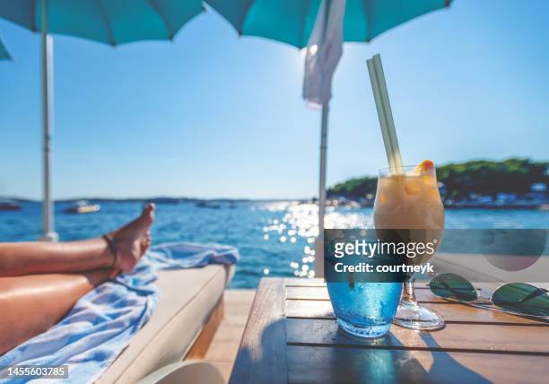 女性の足が見える水辺のカクテルとサングラス - 2 coconut drinks ストックフォトと画像