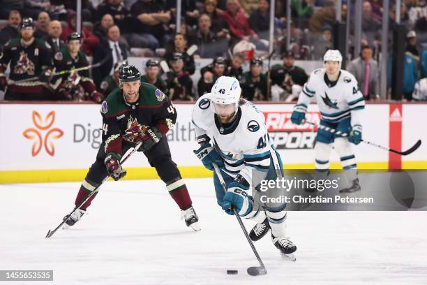 Jonah Gadjovich of the San Jose Sharks skates with the puck ahead of Zack Kassian of the Arizona Coyotes during the third period of the NHL game at...